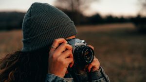 Persoon met grijze muts fotografeert buiten met een Canon-camera bij zonsondergang – beeldoptimalisatie in actie