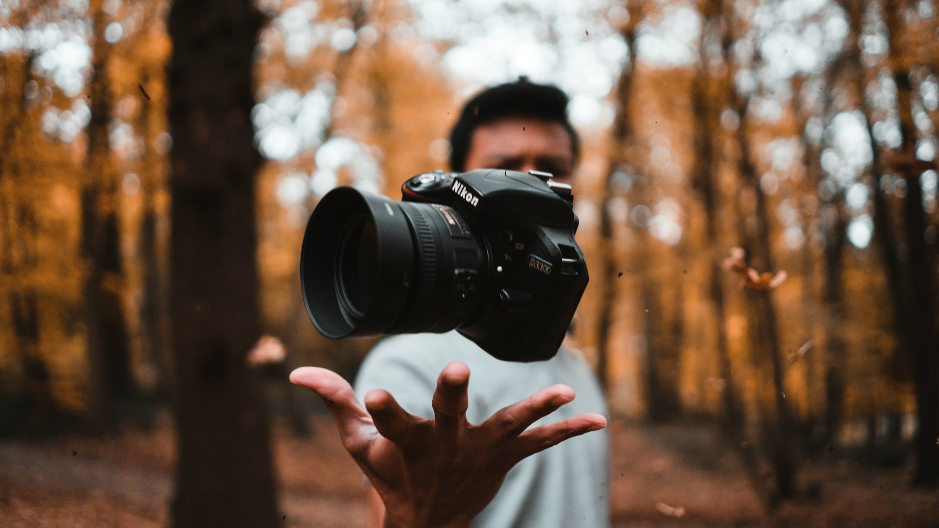 Zwevende Nikon-camera boven hand van persoon in herfstbos, focus op camera en onscherpe achtergrond