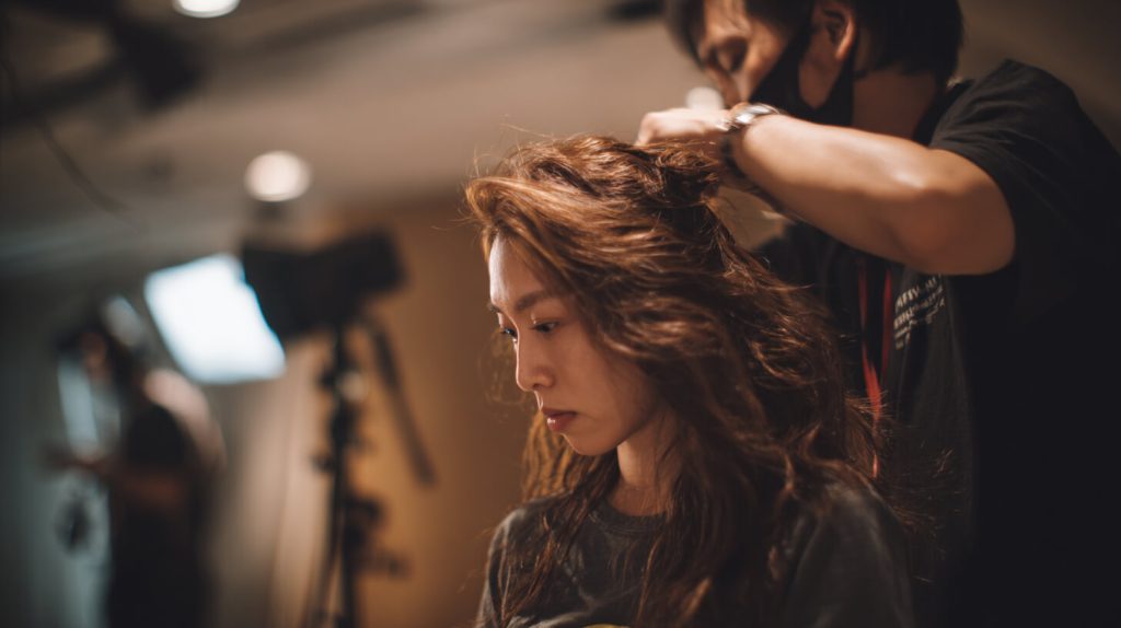 Voorbereiding van haar voor een professionele portretfoto met aandacht voor volume en styling.